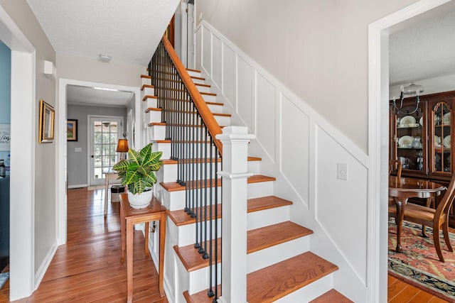 stairs featuring a decorative wall, a textured ceiling, baseboards, and wood finished floors