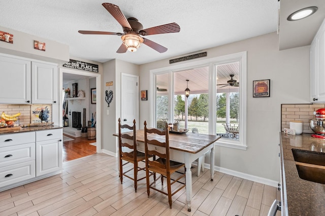 dining area featuring light wood finished floors, ceiling fan, baseboards, and a textured ceiling