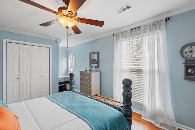 bedroom featuring wood finished floors, visible vents, baseboards, ornamental molding, and a closet
