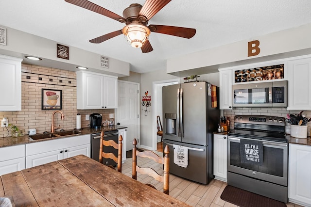 kitchen with white cabinets, a sink, stainless steel appliances, light wood-style floors, and backsplash