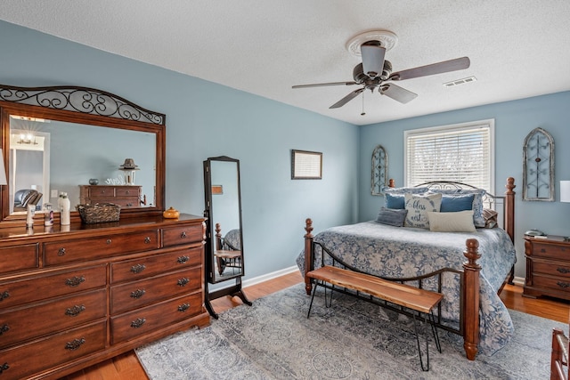 bedroom with a ceiling fan, light wood-style flooring, visible vents, and a textured ceiling