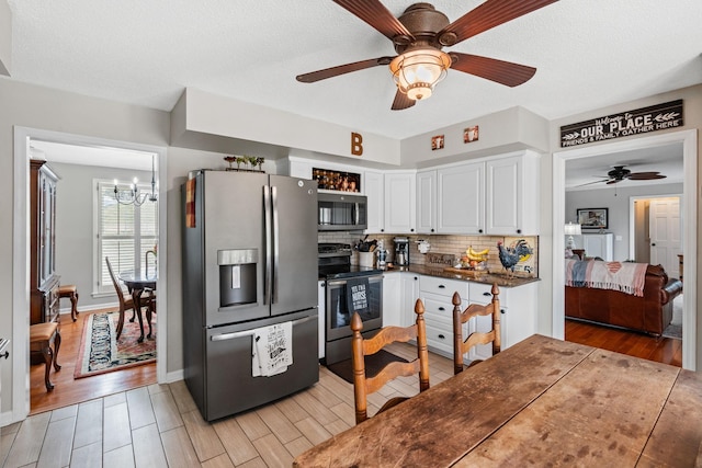 kitchen featuring dark countertops, decorative backsplash, appliances with stainless steel finishes, white cabinetry, and light wood-type flooring