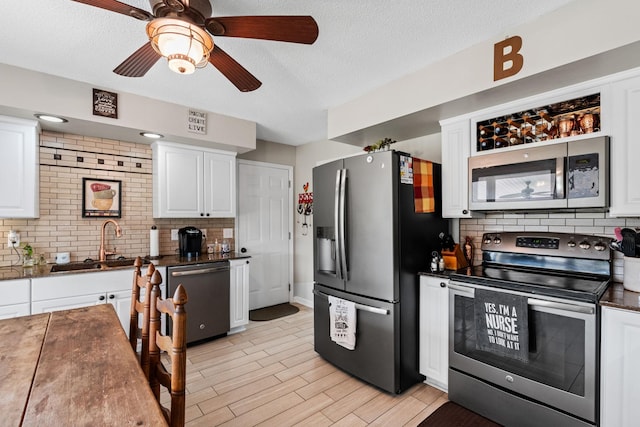 kitchen with appliances with stainless steel finishes, dark countertops, a sink, and white cabinetry