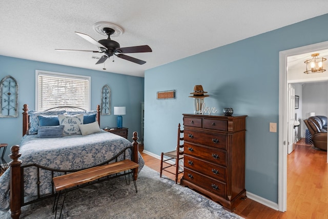 bedroom with ceiling fan, a textured ceiling, baseboards, and wood finished floors