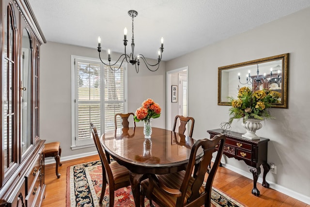 dining area featuring light wood-style floors, a textured ceiling, baseboards, and an inviting chandelier