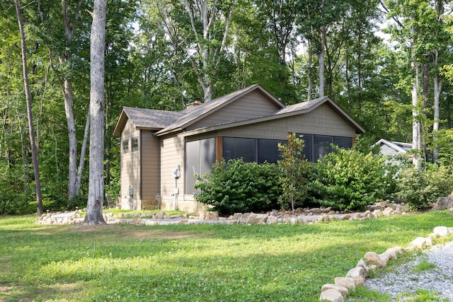 view of property exterior featuring a sunroom, roof with shingles, a chimney, and a yard