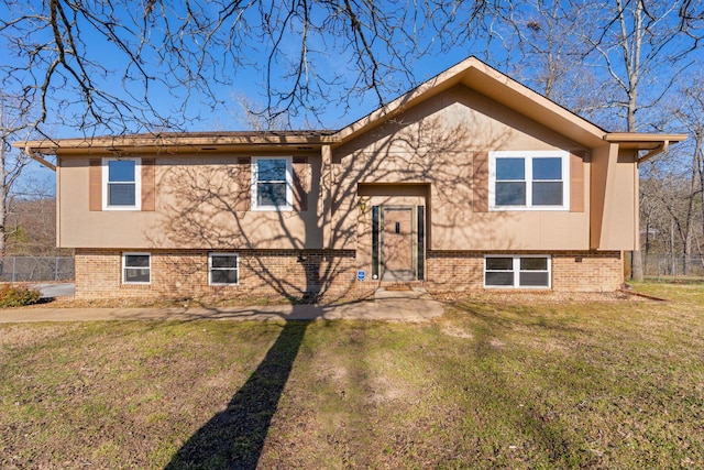 bi-level home featuring stucco siding, fence, a front lawn, and brick siding