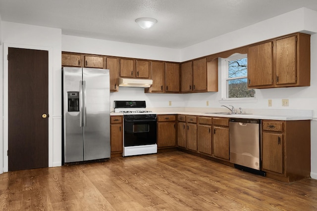 kitchen featuring dark wood-style flooring, stainless steel appliances, light countertops, a sink, and under cabinet range hood