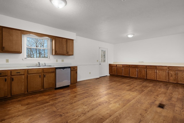 kitchen with visible vents, dark wood-style flooring, light countertops, stainless steel dishwasher, and a sink