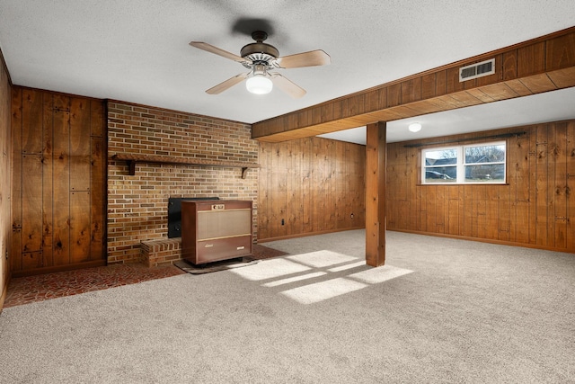 basement featuring a textured ceiling, wooden walls, visible vents, carpet, and a wood stove