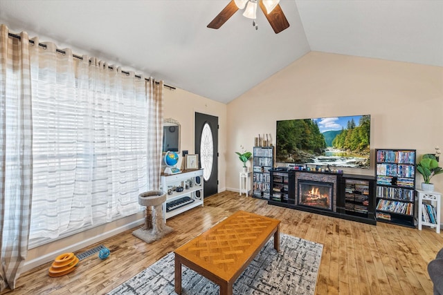 living room featuring lofted ceiling, a ceiling fan, wood finished floors, a warm lit fireplace, and baseboards