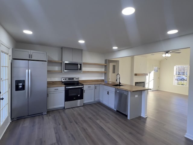 kitchen featuring wood counters, appliances with stainless steel finishes, a peninsula, open shelves, and a sink