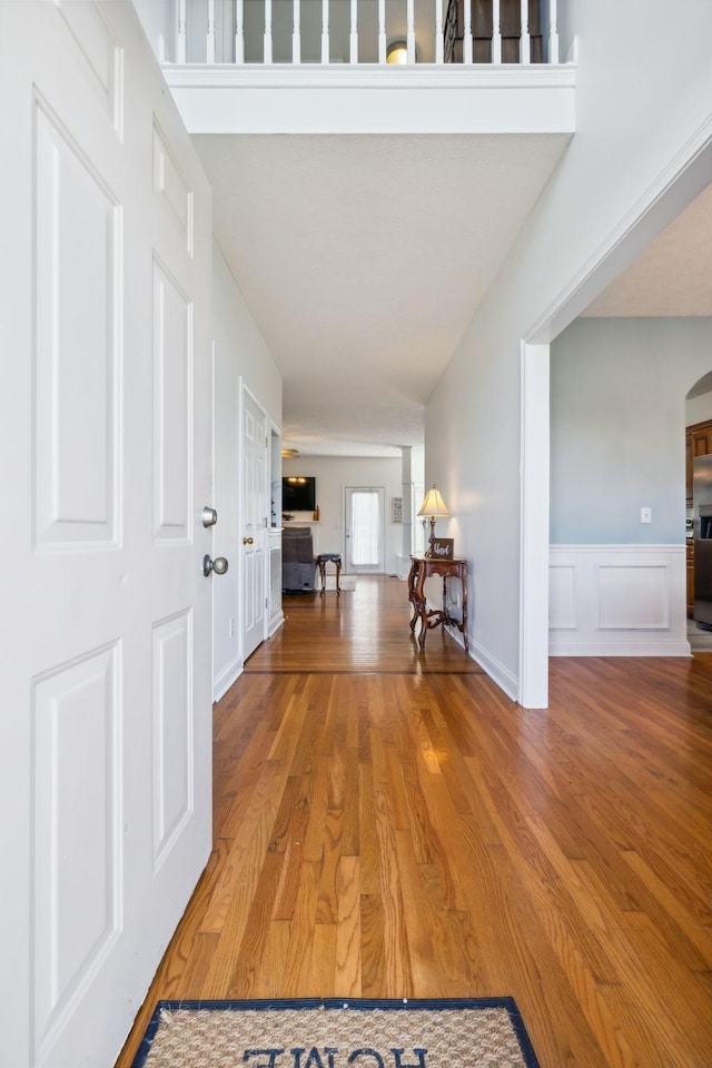 hallway with a wainscoted wall, arched walkways, a decorative wall, and wood finished floors