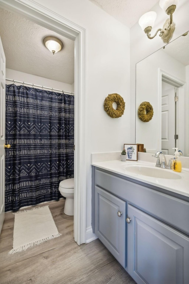 bathroom with a textured ceiling, vanity, wood finished floors, and toilet