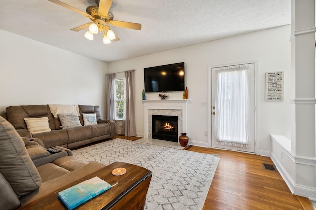 living area with visible vents, a ceiling fan, wood finished floors, a textured ceiling, and a high end fireplace