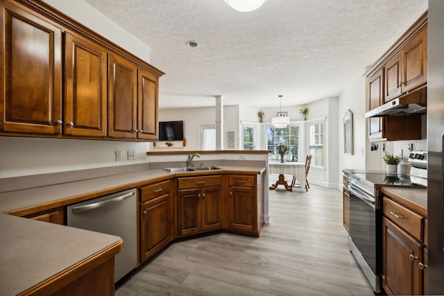 kitchen with a peninsula, stainless steel appliances, light wood-type flooring, under cabinet range hood, and a sink