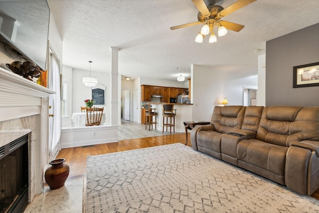 living area featuring a fireplace, a textured ceiling, light wood finished floors, and ceiling fan