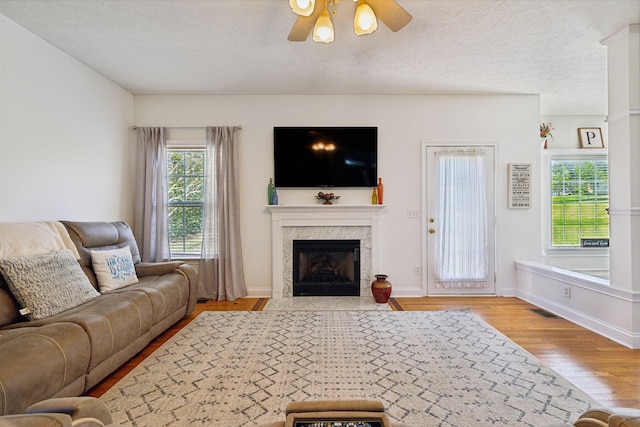 living area featuring visible vents, a ceiling fan, a tiled fireplace, wood finished floors, and a textured ceiling