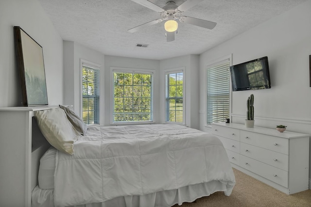 carpeted bedroom with a textured ceiling, multiple windows, visible vents, and a ceiling fan