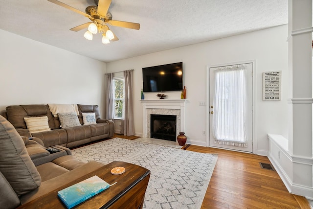 living area with a fireplace, visible vents, a ceiling fan, a textured ceiling, and wood finished floors