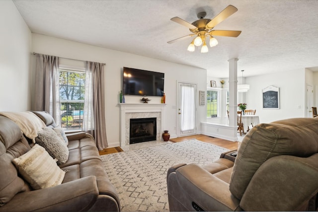 living room with a textured ceiling, a fireplace with flush hearth, wood finished floors, a ceiling fan, and baseboards