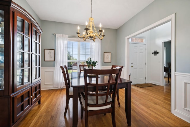 dining space featuring a wainscoted wall, a decorative wall, an inviting chandelier, and wood finished floors