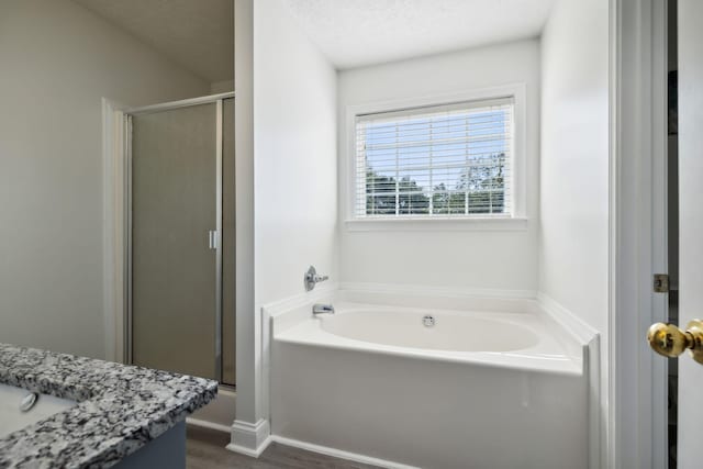 bathroom featuring a textured ceiling, wood finished floors, vanity, a bath, and a stall shower