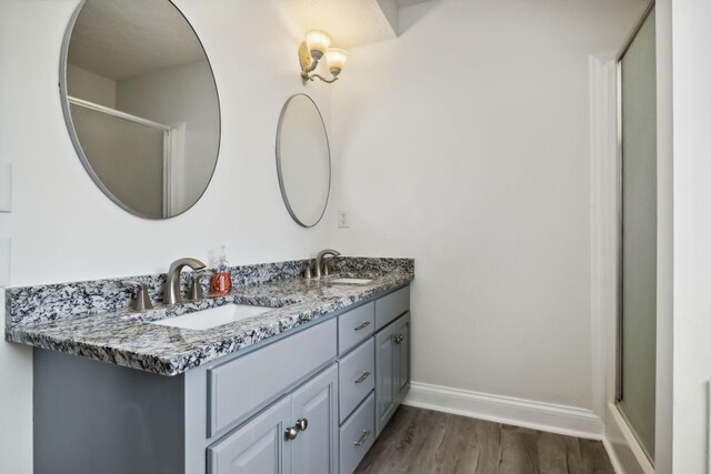 full bathroom featuring double vanity, wood finished floors, a sink, and baseboards