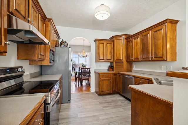 kitchen with arched walkways, appliances with stainless steel finishes, brown cabinets, and under cabinet range hood