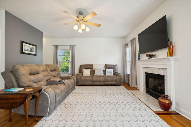 living room with light wood-style flooring, baseboards, ceiling fan, and a high end fireplace