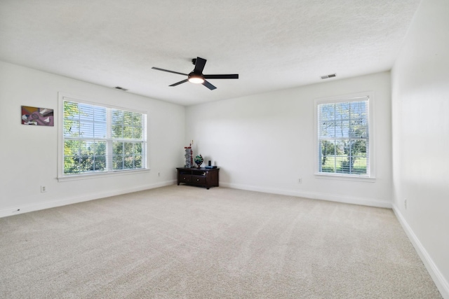 spare room with a textured ceiling, carpet flooring, visible vents, and a healthy amount of sunlight