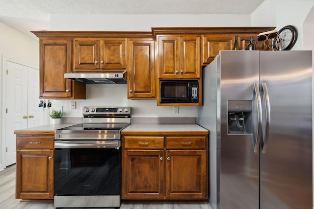 kitchen featuring light wood finished floors, light countertops, appliances with stainless steel finishes, brown cabinetry, and under cabinet range hood