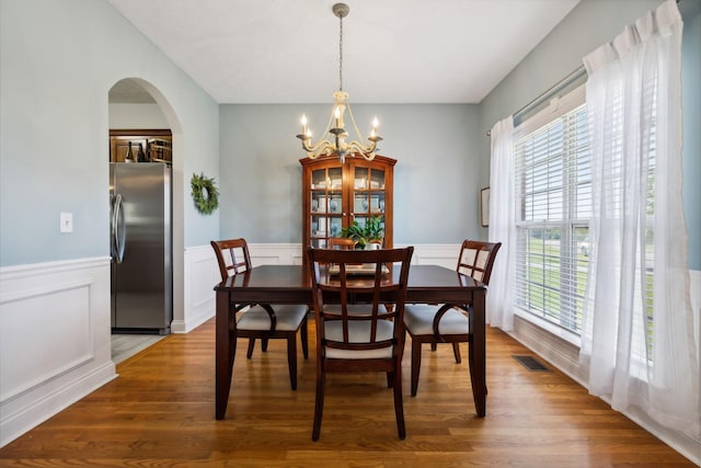 dining room featuring arched walkways, visible vents, an inviting chandelier, and wood finished floors