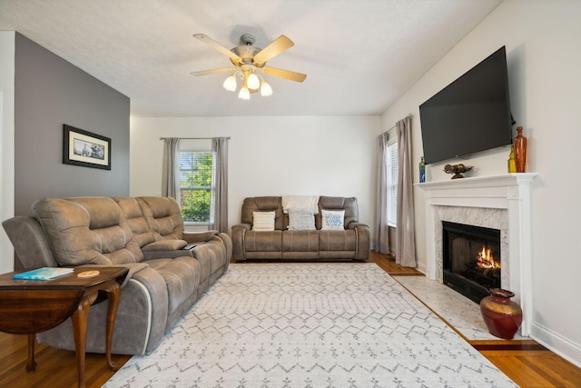 living room with light wood finished floors, a premium fireplace, baseboards, and a ceiling fan