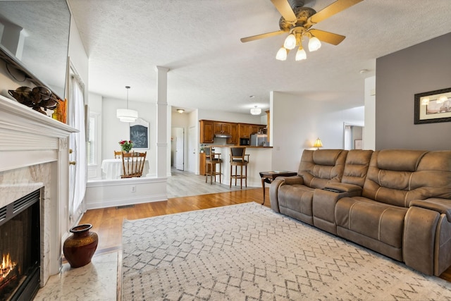 living area with a ceiling fan, a fireplace, light wood-style flooring, and a textured ceiling