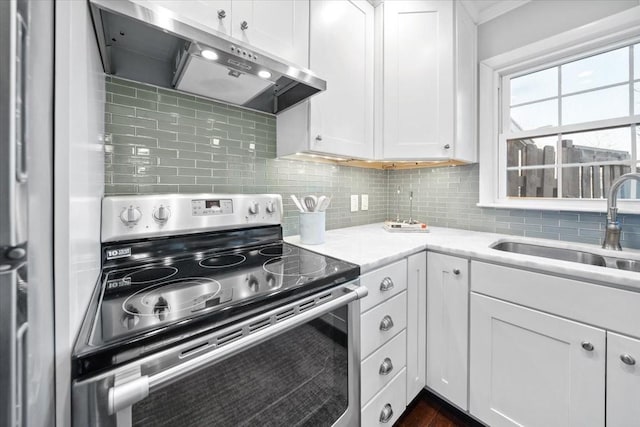 kitchen with tasteful backsplash, white cabinets, stainless steel range with electric cooktop, a sink, and under cabinet range hood