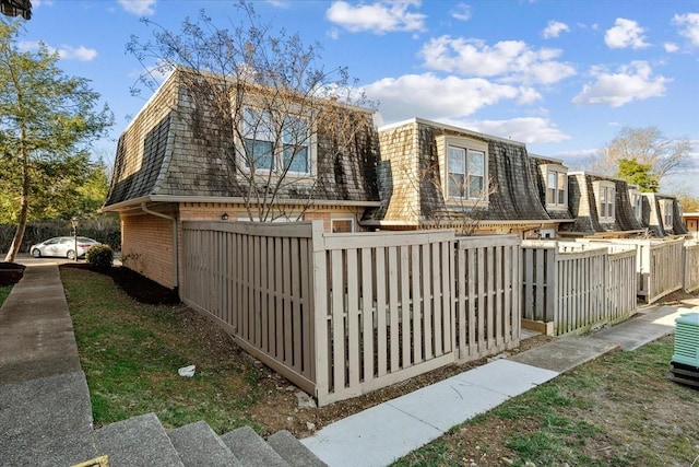 view of front of house with mansard roof, a fenced front yard, a shingled roof, and brick siding