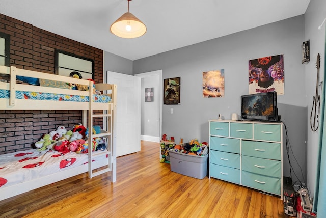 bedroom with light wood-style floors and brick wall