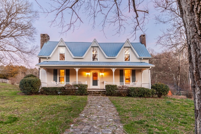 view of front facade with covered porch, a chimney, and a lawn