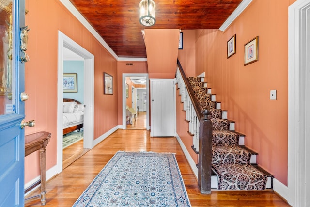 foyer entrance featuring ornamental molding, wood ceiling, light wood-style flooring, and stairs