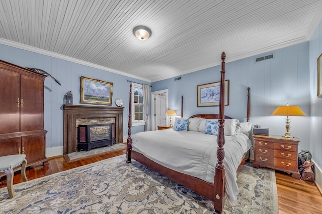 bedroom featuring a fireplace with raised hearth, wood finished floors, visible vents, and crown molding