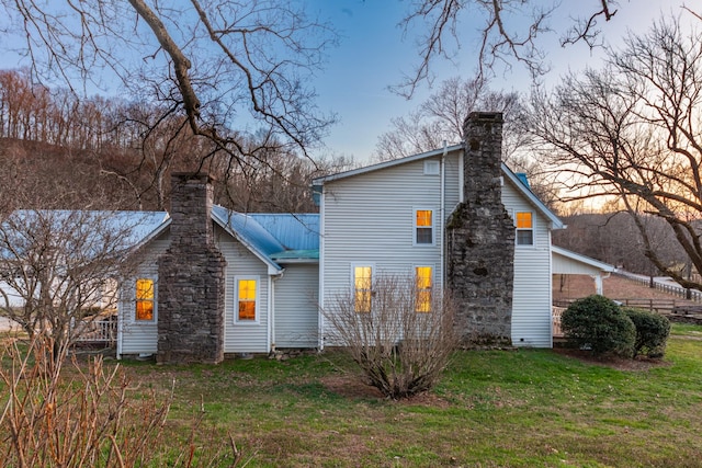 property exterior at dusk featuring metal roof, a yard, and a chimney