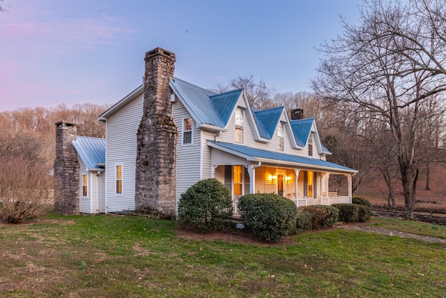 property exterior at dusk with metal roof, covered porch, a lawn, and a chimney