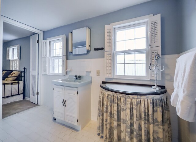 bathroom featuring a tub, wainscoting, tile walls, and vanity