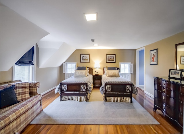 bedroom with vaulted ceiling, wood finished floors, visible vents, and baseboards