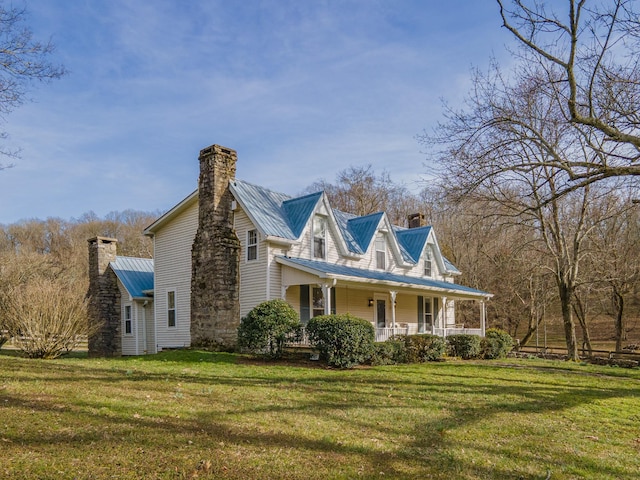 view of front of home featuring a front yard, a chimney, metal roof, and a porch