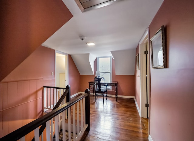 hallway featuring lofted ceiling, baseboards, wood finished floors, and an upstairs landing