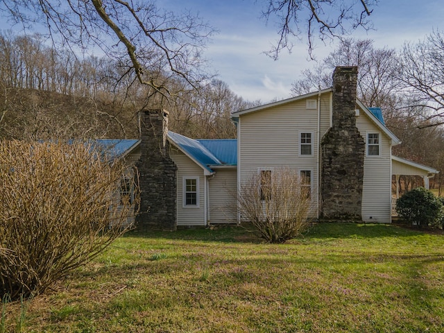 rear view of house featuring a chimney, metal roof, and a lawn