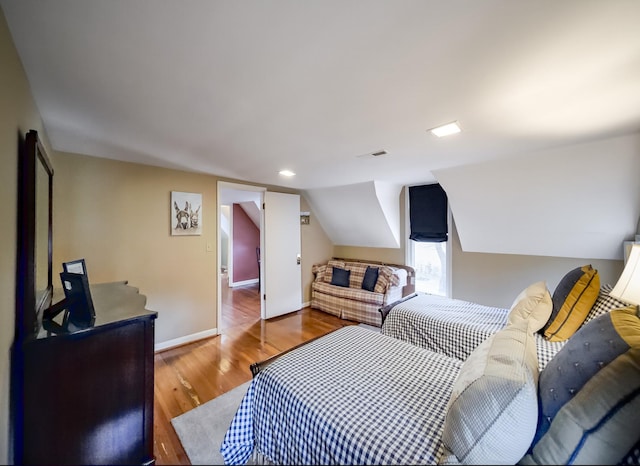 bedroom with lofted ceiling, visible vents, baseboards, and wood finished floors