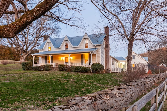 view of front facade featuring a chimney, metal roof, covered porch, fence, and a front lawn